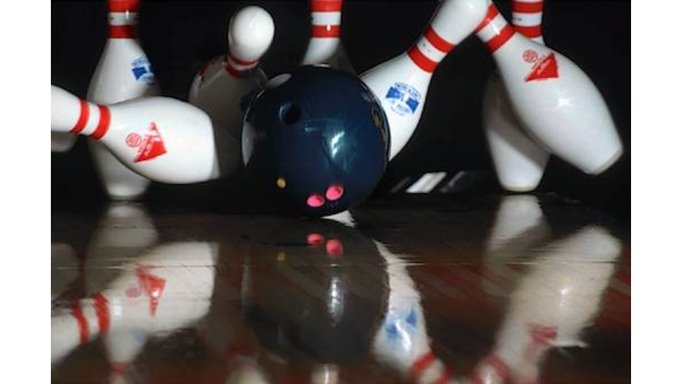 white and red bowling pins being hit by black bowling ball - all reflected in shiny wood floor